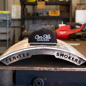 Black cap with 'Cen-Tex Smokers' logo on a metal object in a workshop setting